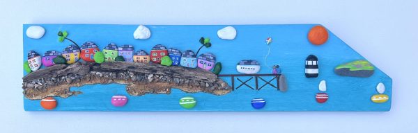 painted pebblescape depicting beaumaris' colourful houses, the pier with a couple on it flying a kite, boats sailing, penmon lighthouse and puffin island with the sun and billowing clouds in the sky by contemporary anglesey artist deborah kempton